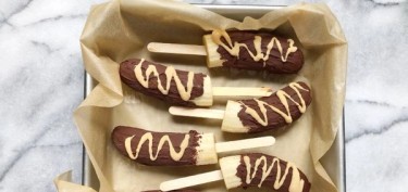 a tray of chocolate covered bananas in a popsicle stick.