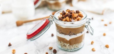 a glass jar filled with layers of granola, peanut butter, yogurt, all topped with chocolate chips and peanuts.
