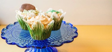 cupcakes holders in the shape of grass topped with creamy peanut butter frosting.