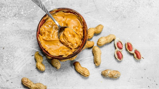 A creamy peanut butter in a bowl next to unshelled peanuts.