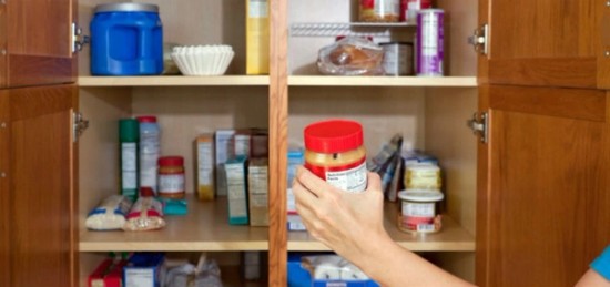 a woman holding a jar of peanut butter in a pantry.