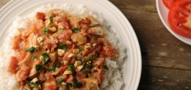 a plate of white rice topped with sauté tomatos and peanuts.