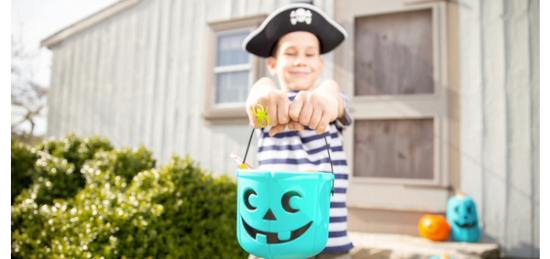 A boy dressed as a pirate is holding a jack o lantern bucket.