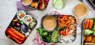 lunch boxes filled with vegetables and containers with dip sauces.