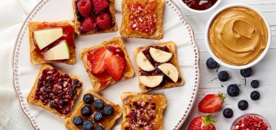 A plate of toasts topped with fruits, jelly and peanut butter.