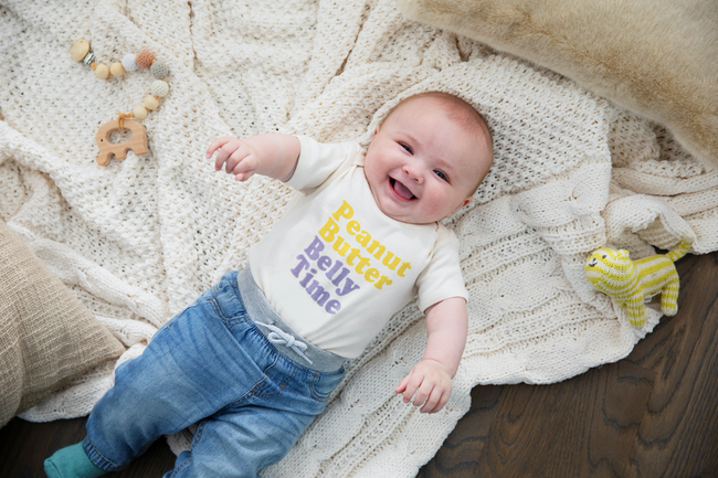 a smiling baby wearing a shirt that says "peanut butter belly time"