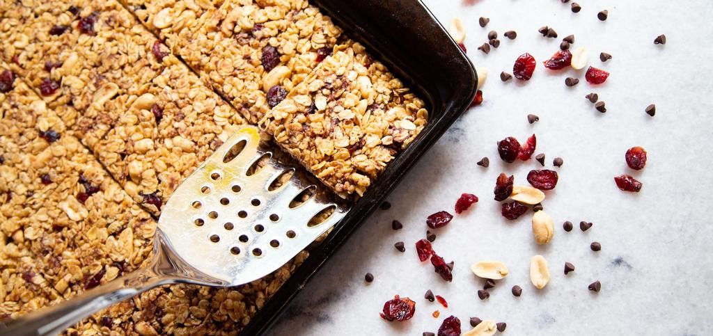 a spoon scooping a square granola bar from a baking tray.