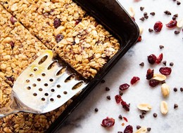 a spoon scooping a square granola bar from a baking tray.