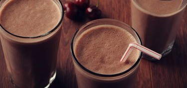 three glasses of chocolate smoothie next to fresh cherries.
