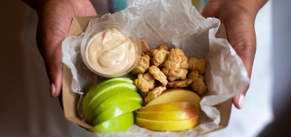 a paper box full of apple slices, kids crackers and a dip sauce.