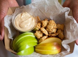 a paper box full of apple slices, kids crackers and a dip sauce.
