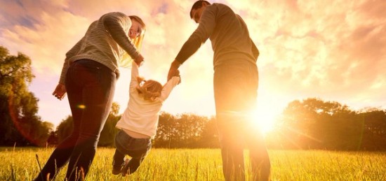 a man and woman holding hands with a kid in a field.