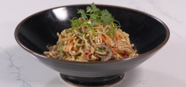 a noodle bowl mixed with vegetables and peanuts.