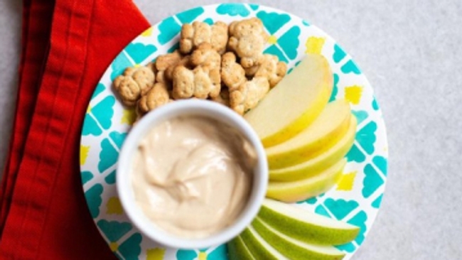 a plate with apples, crackers and a bowl of peanut butter.