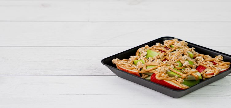 a bowl of cutted fruits glazed with peanut butter.