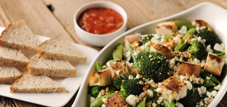 a bowl of broccoli, cauliflower, and bread on a table.