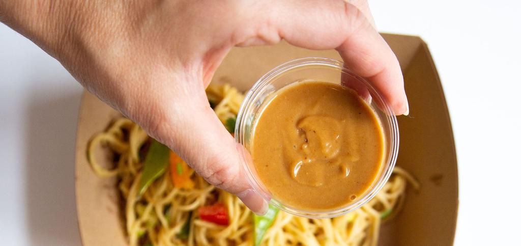 a person holding a container of sauce over a plate of pasta.
