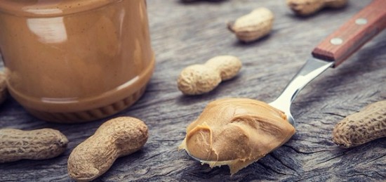 spoon full of peanut butter next to a few unshelled peanuts.