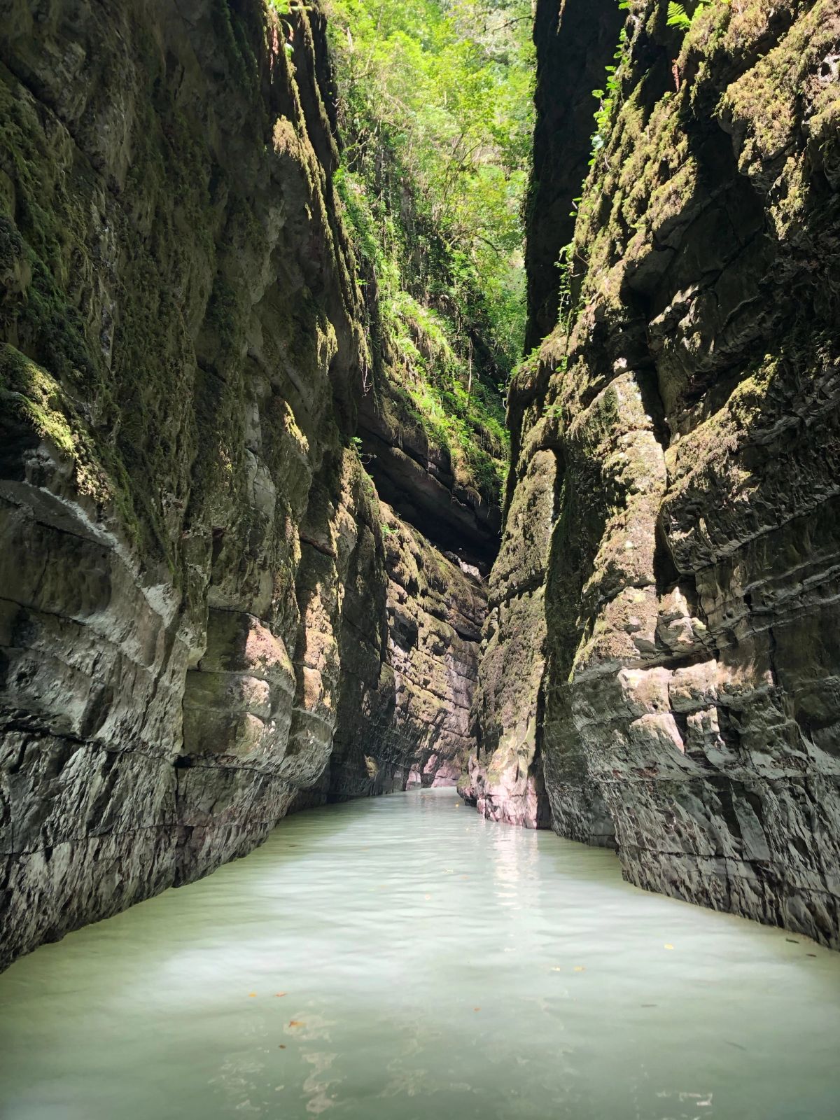 Bamboo raft on dark green water between the tall rock walls of Debotakhum