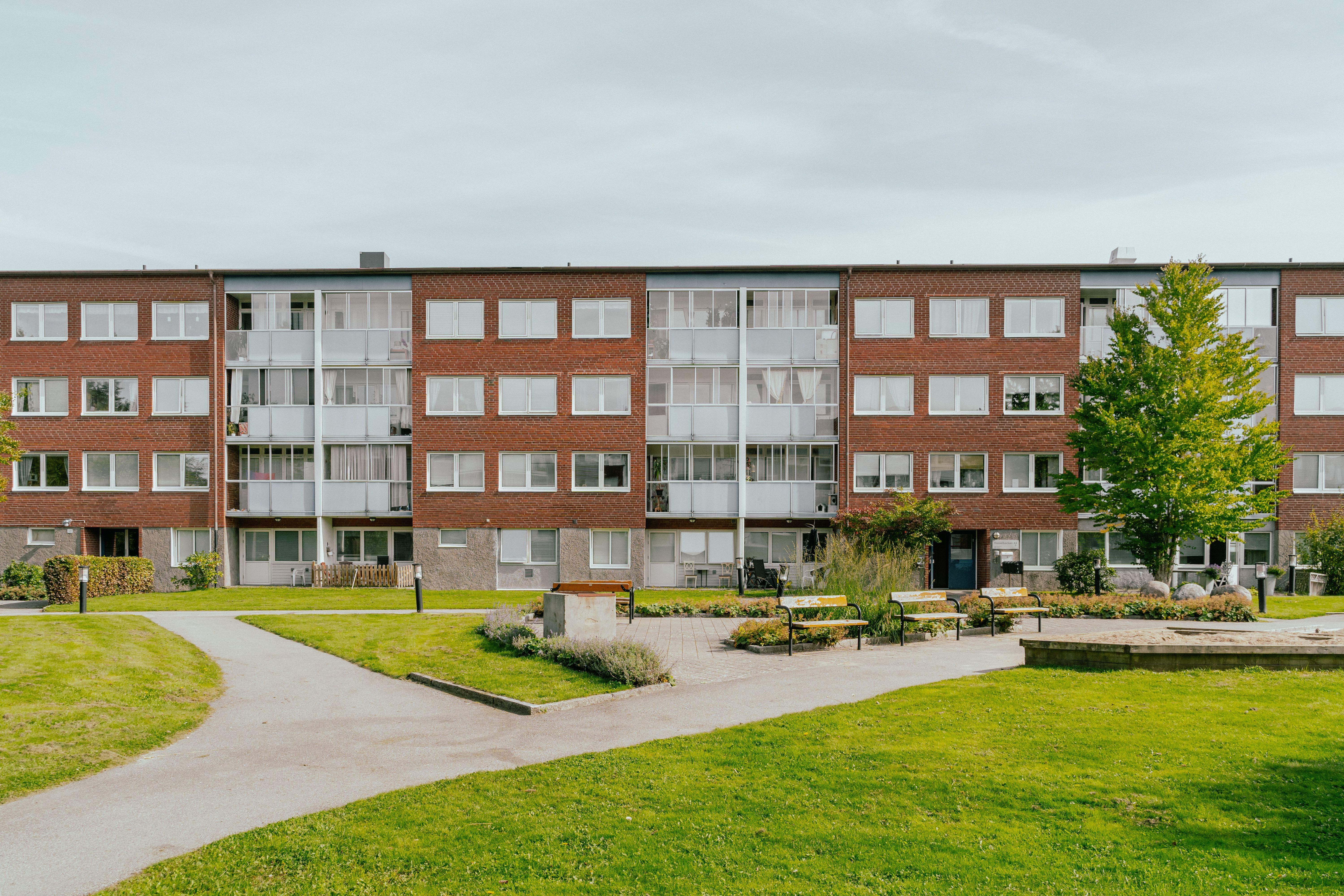 Stor gård med gräsmattor och parkbänkar framför ett lägenhetshus