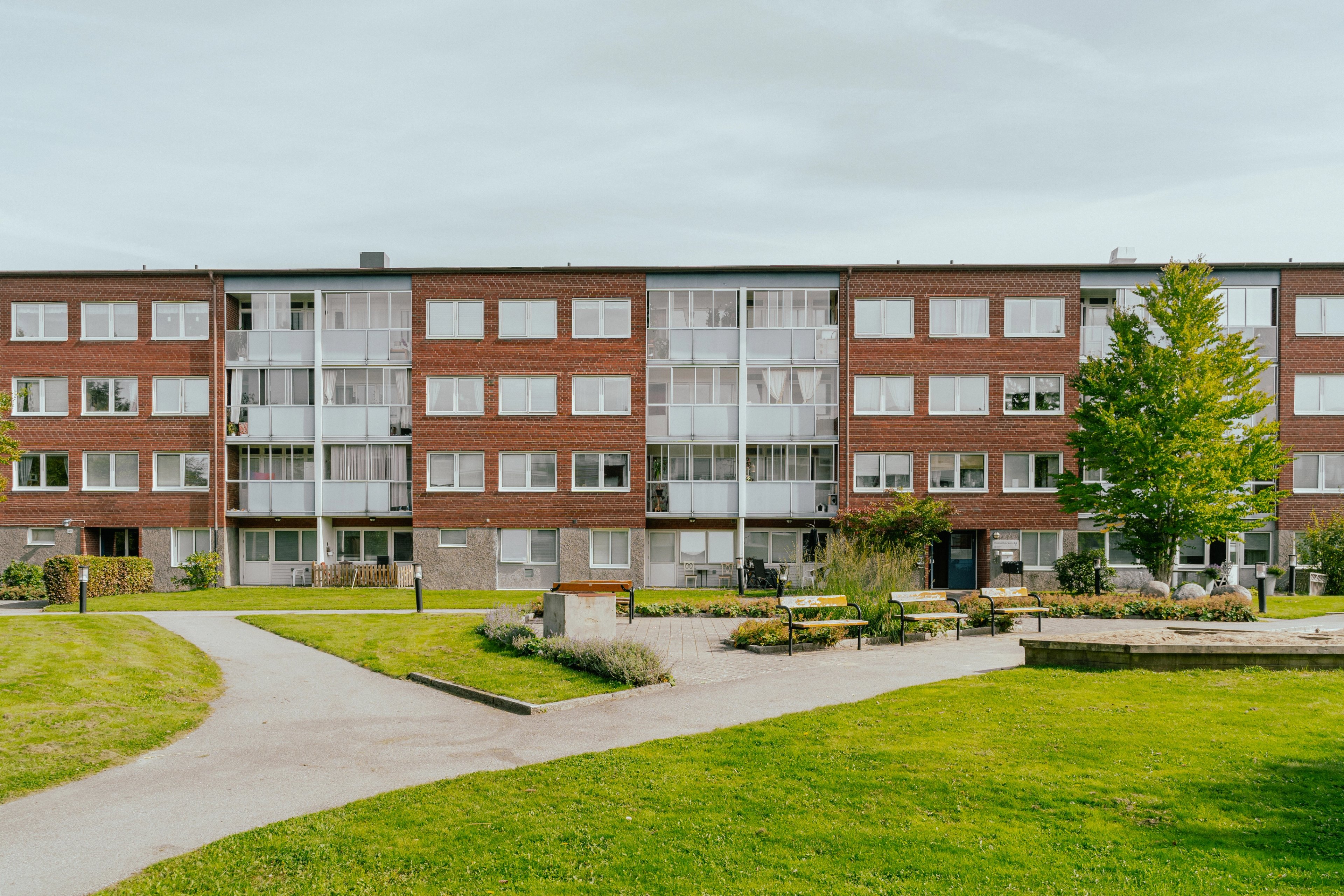 Stor gård med gräsmattor och parkbänkar framför ett lägenhetshus