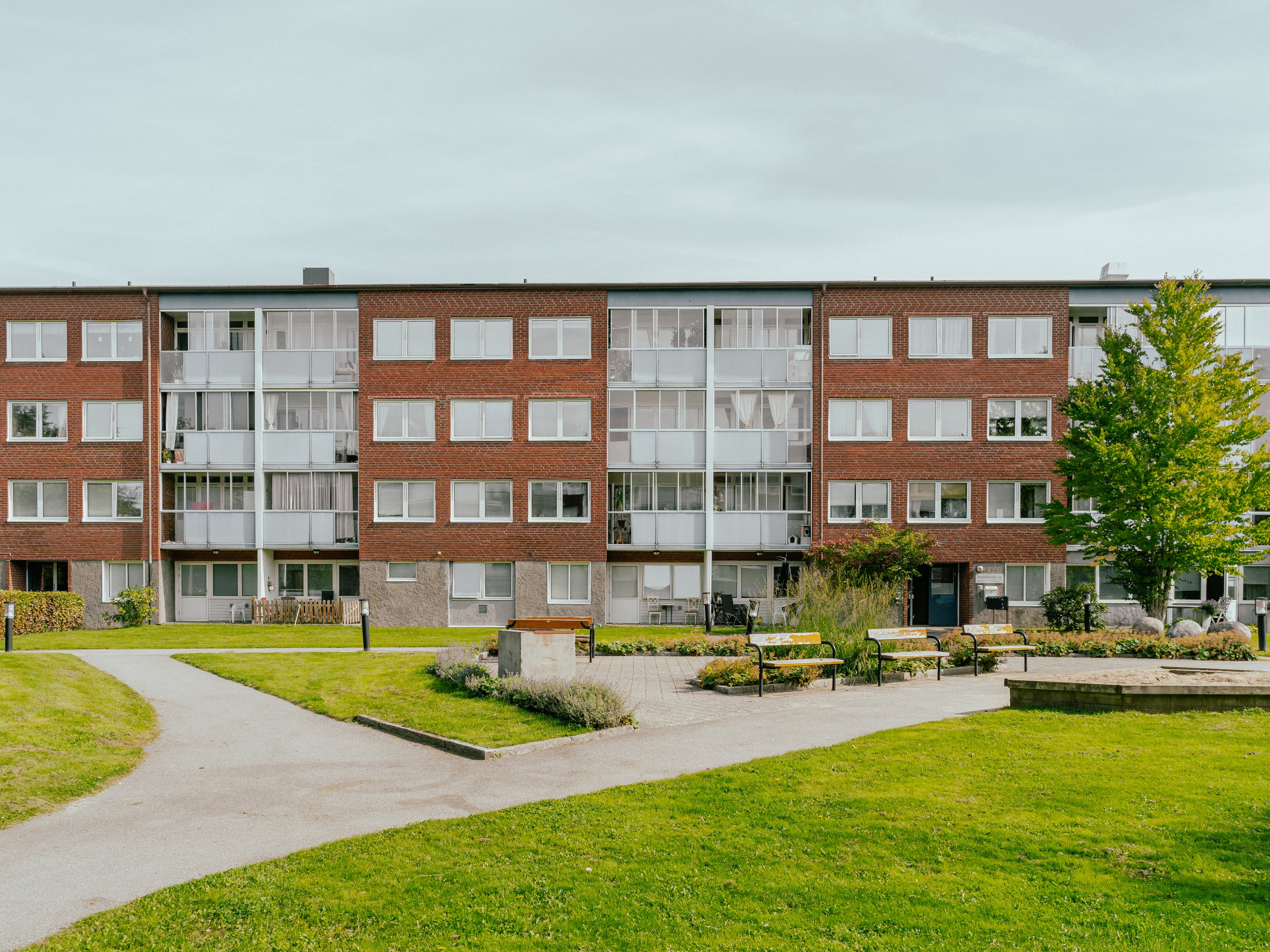 Stor gård med gräsmattor och parkbänkar framför ett lägenhetshus