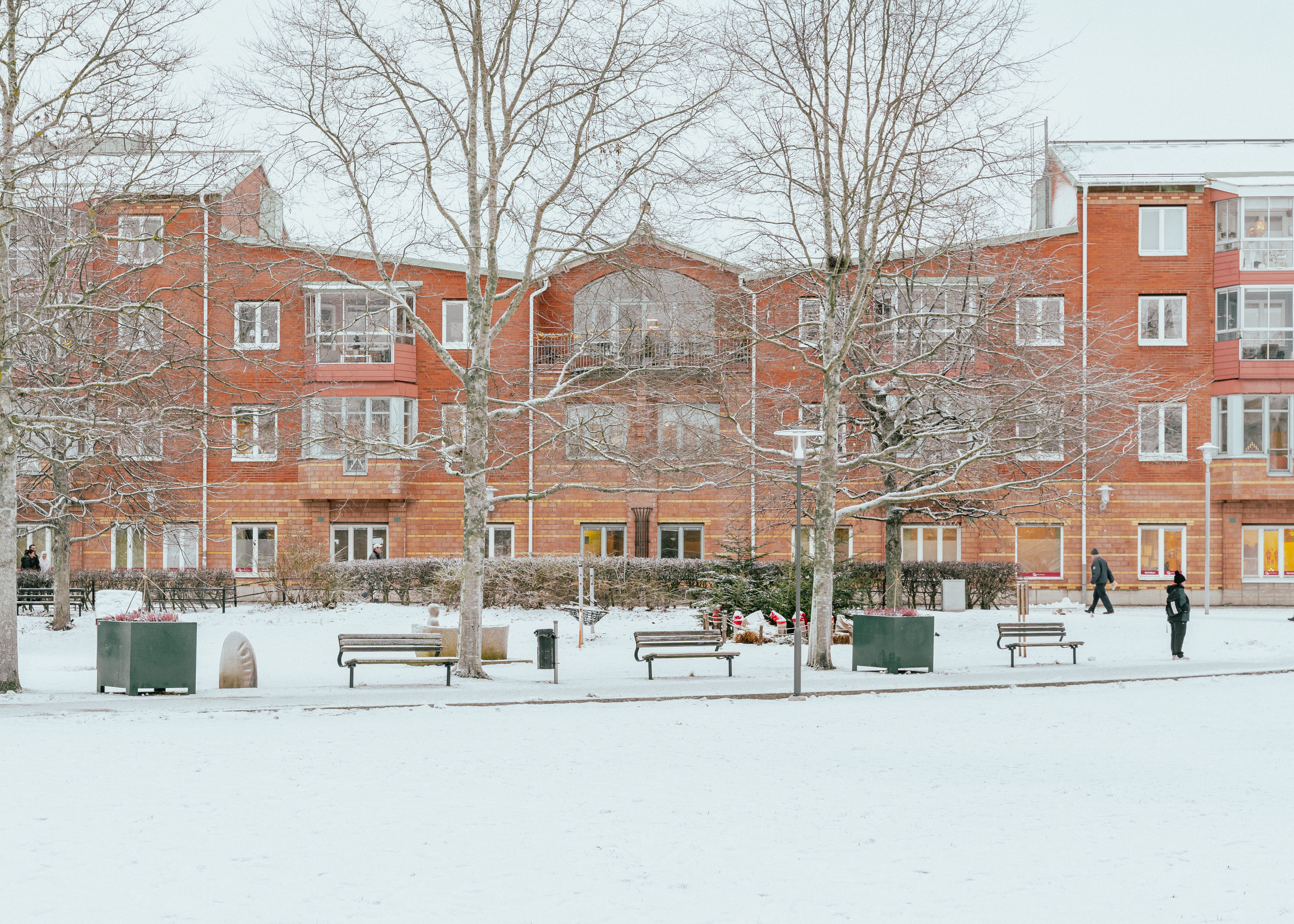 Husfasad från avstånd med träd och bänkar framför