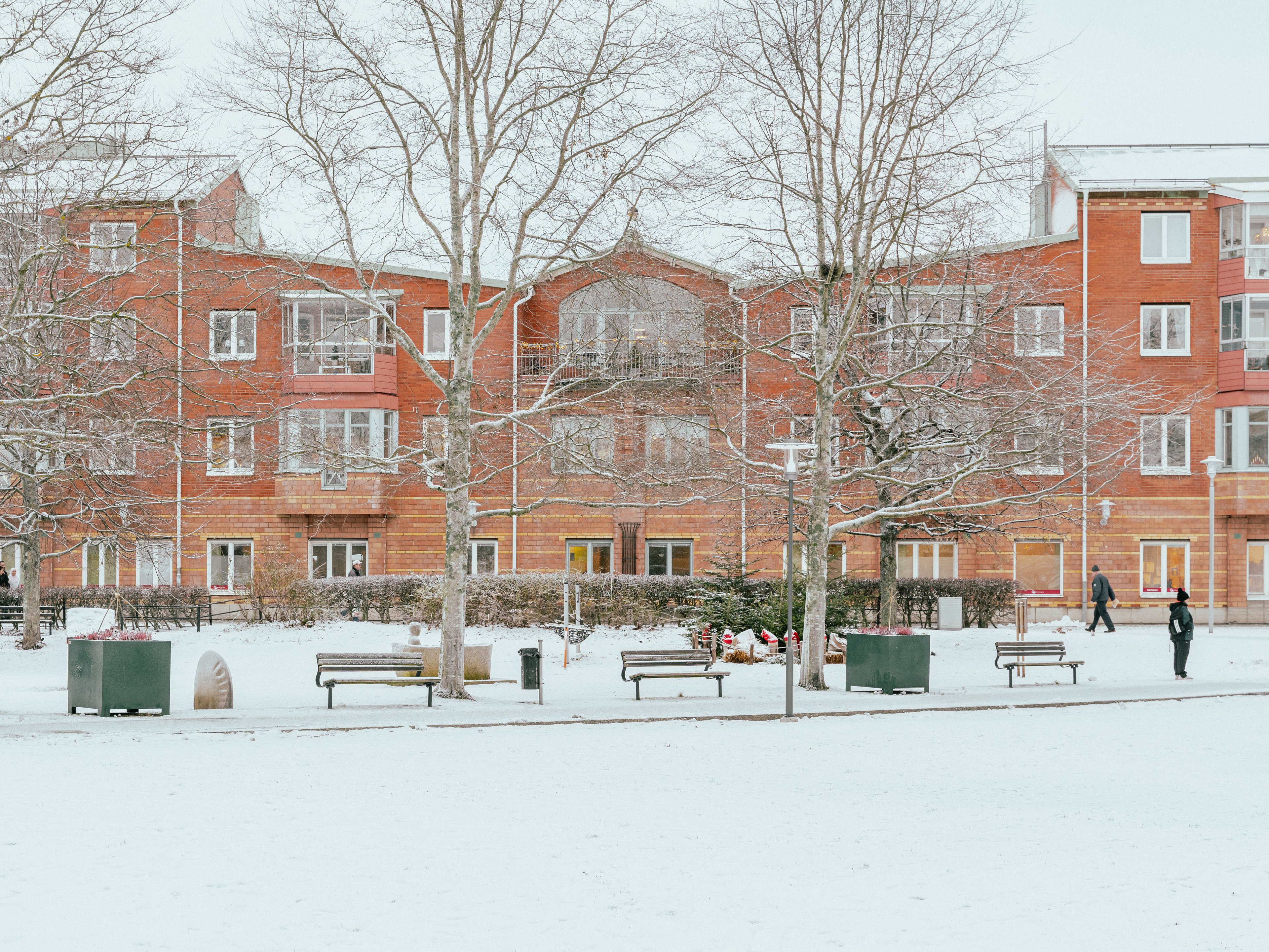Husfasad från avstånd med träd och bänkar framför