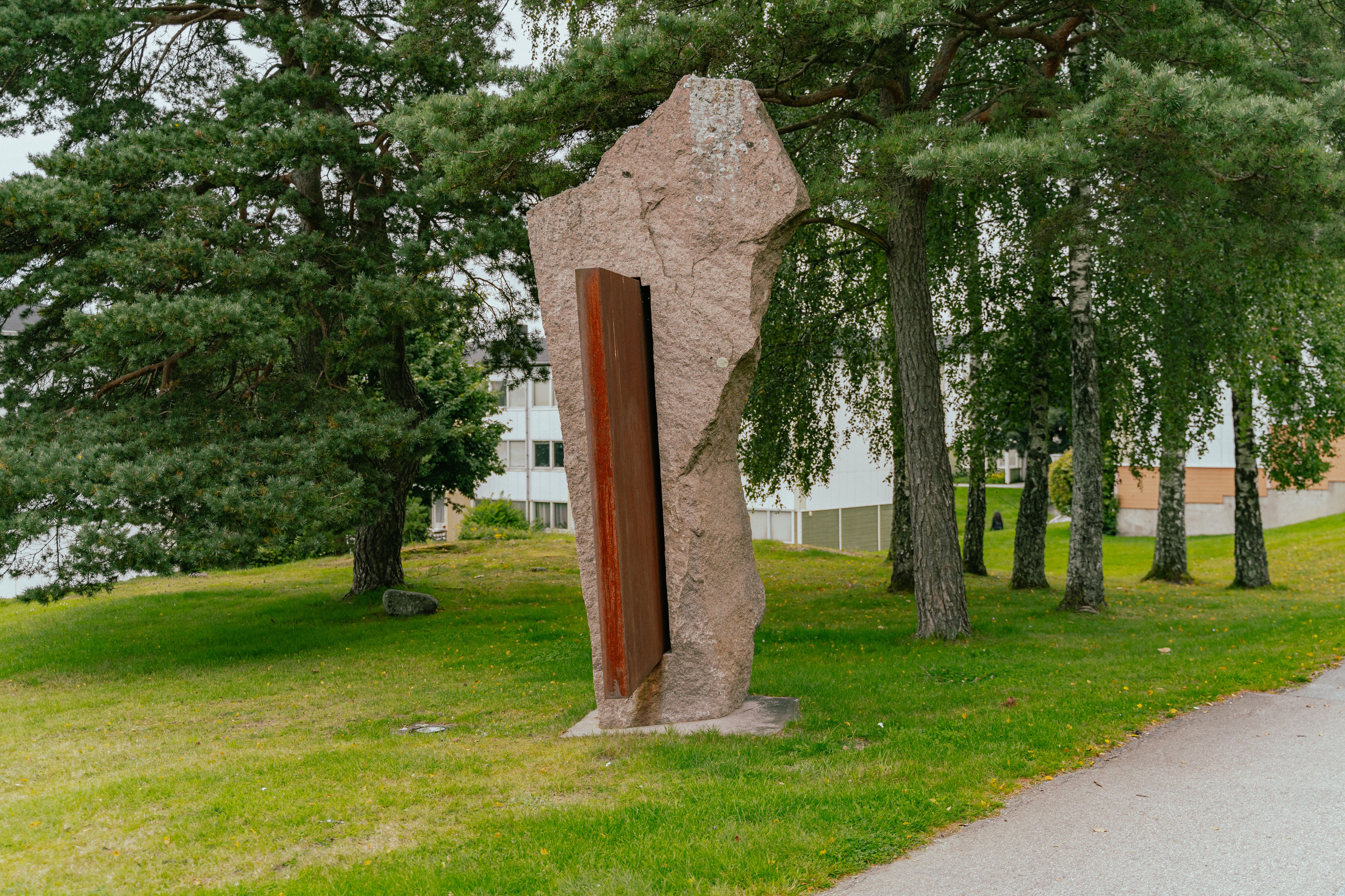 Ett konstverk i granit och stål bland träd och gräsmatta