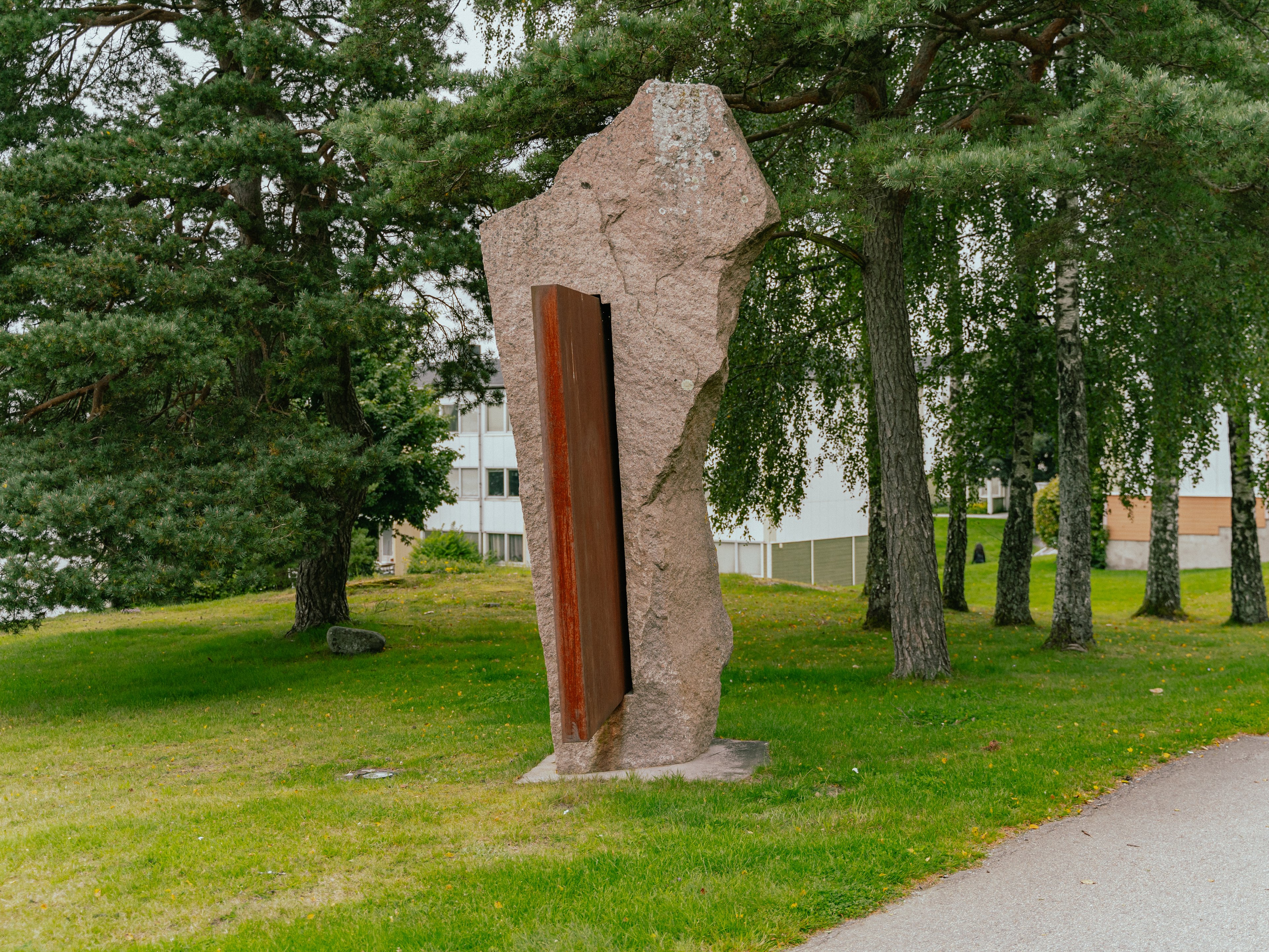Ett konstverk i granit och stål bland träd och gräsmatta