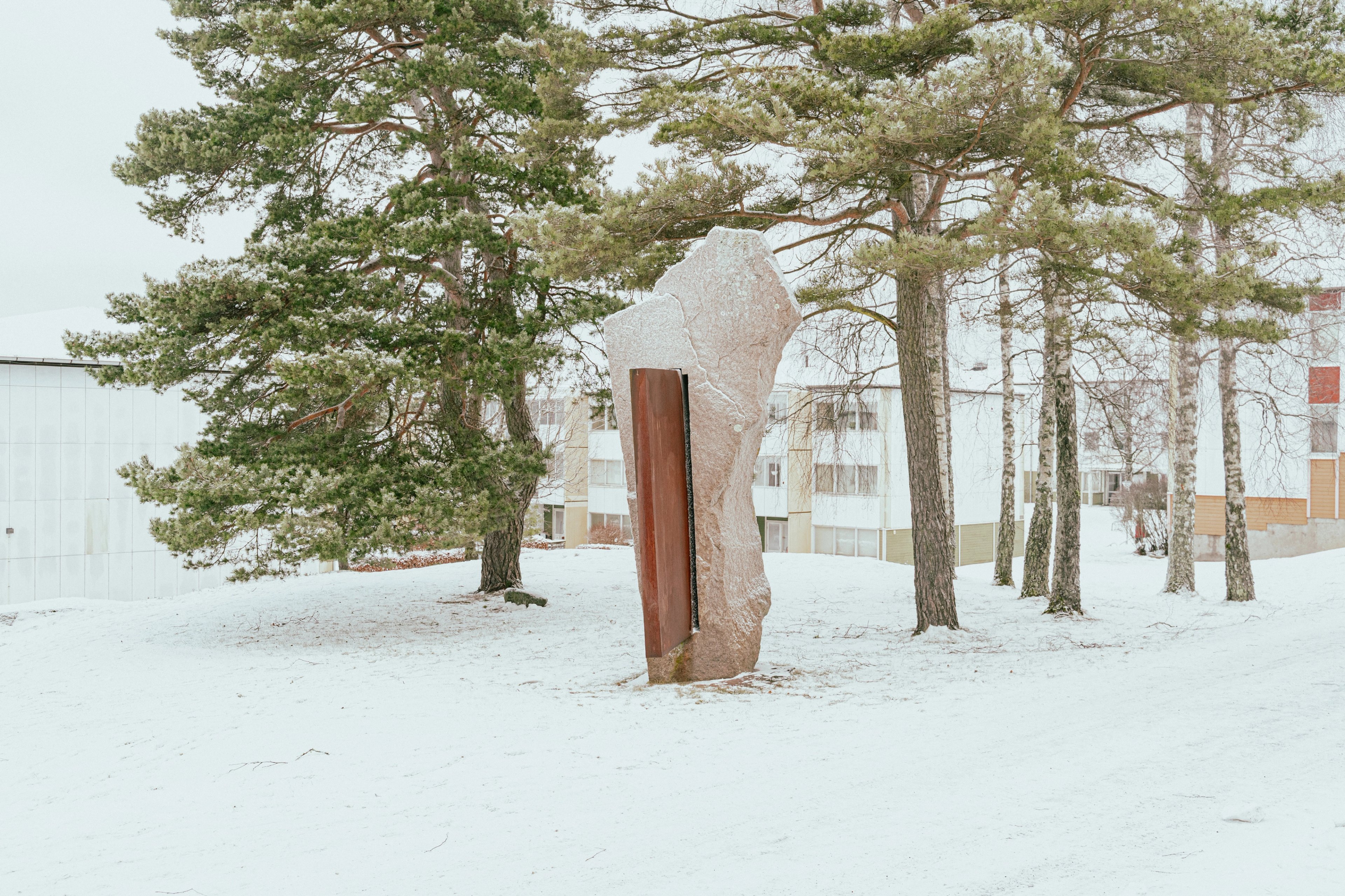 Ett konstverk i granit och stål bland träd och snö