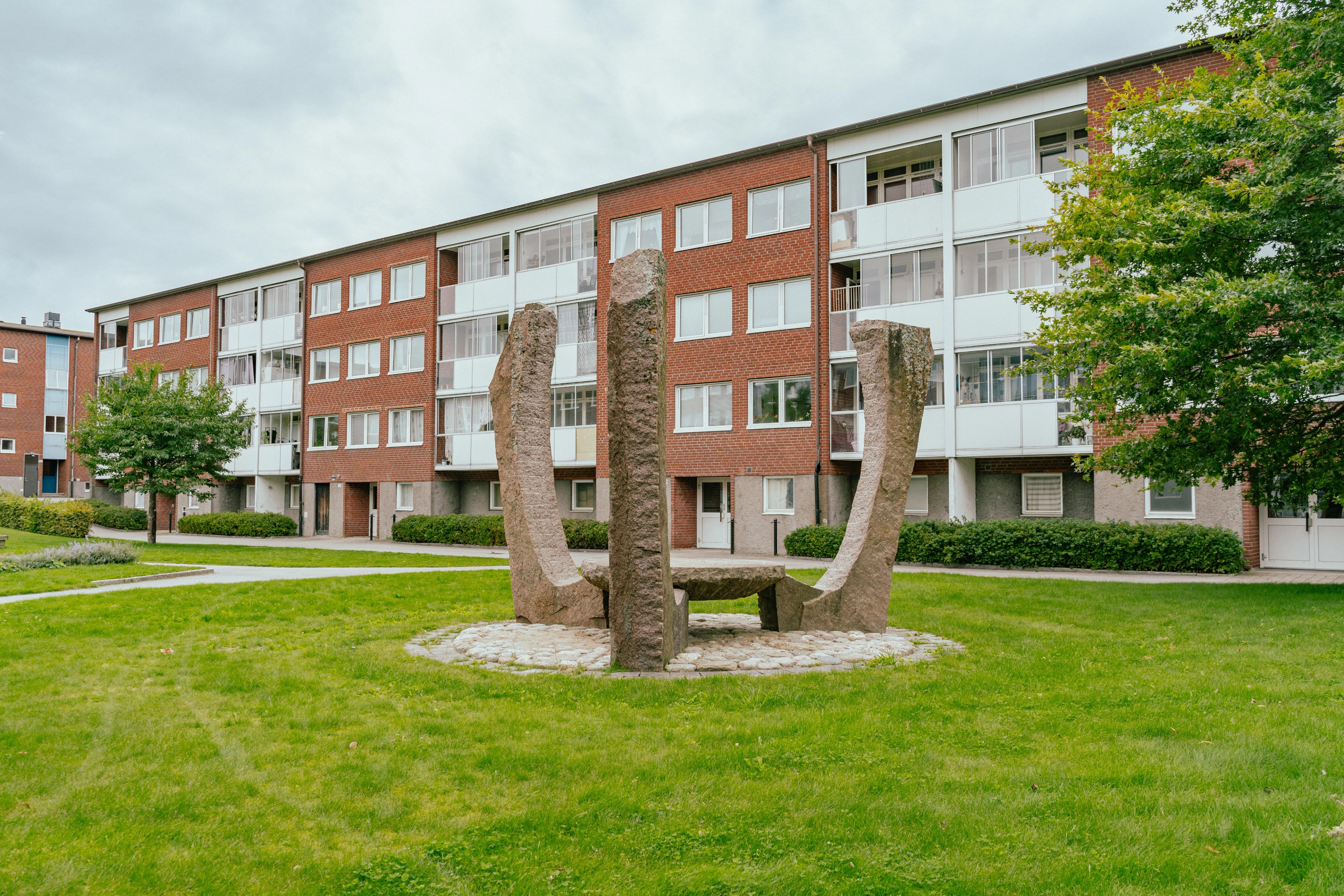 Ett stort konstverk i granit på en gräsmatta mellan hyreshus
