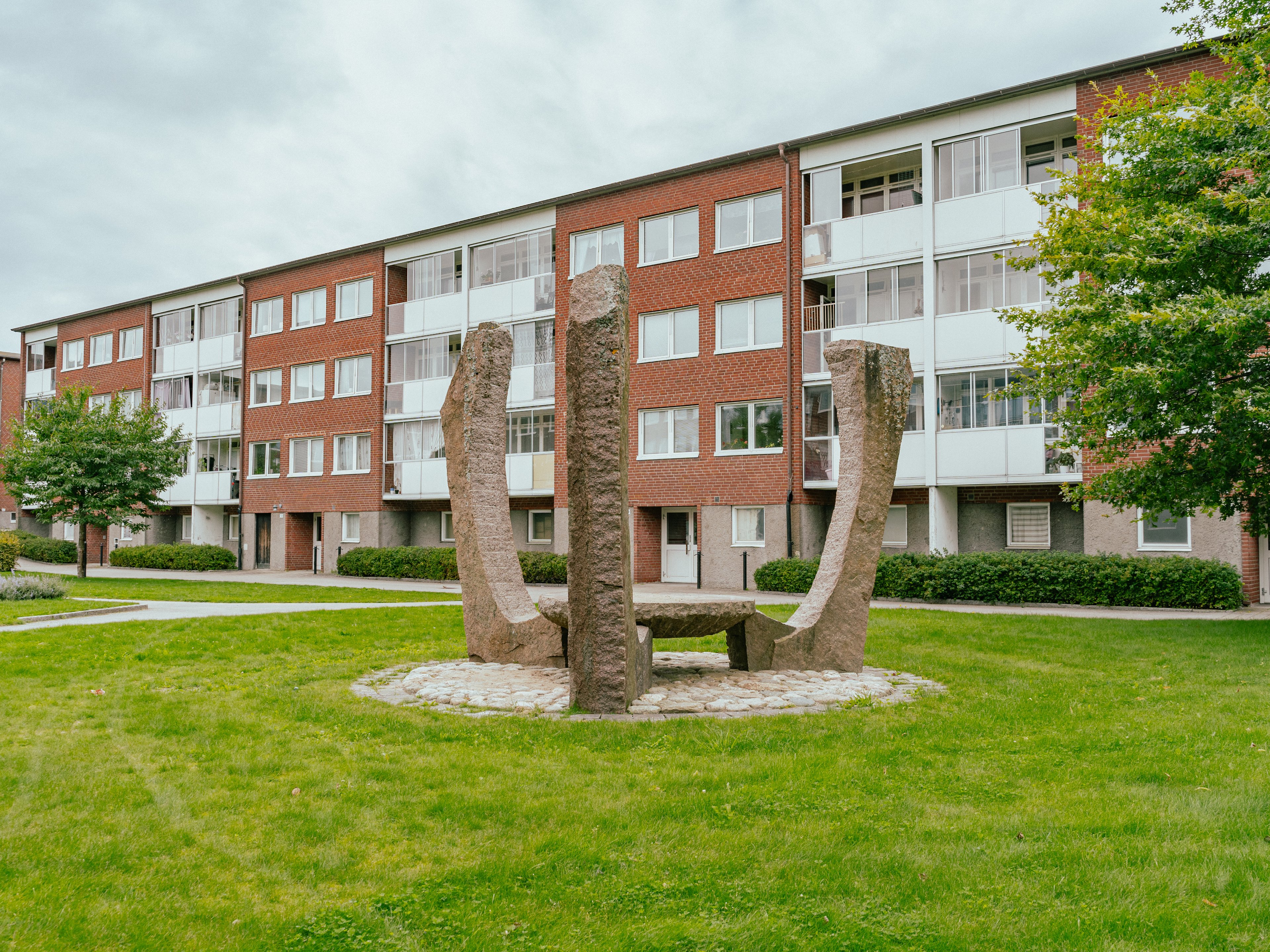 Ett stort konstverk i granit på en gräsmatta mellan hyreshus