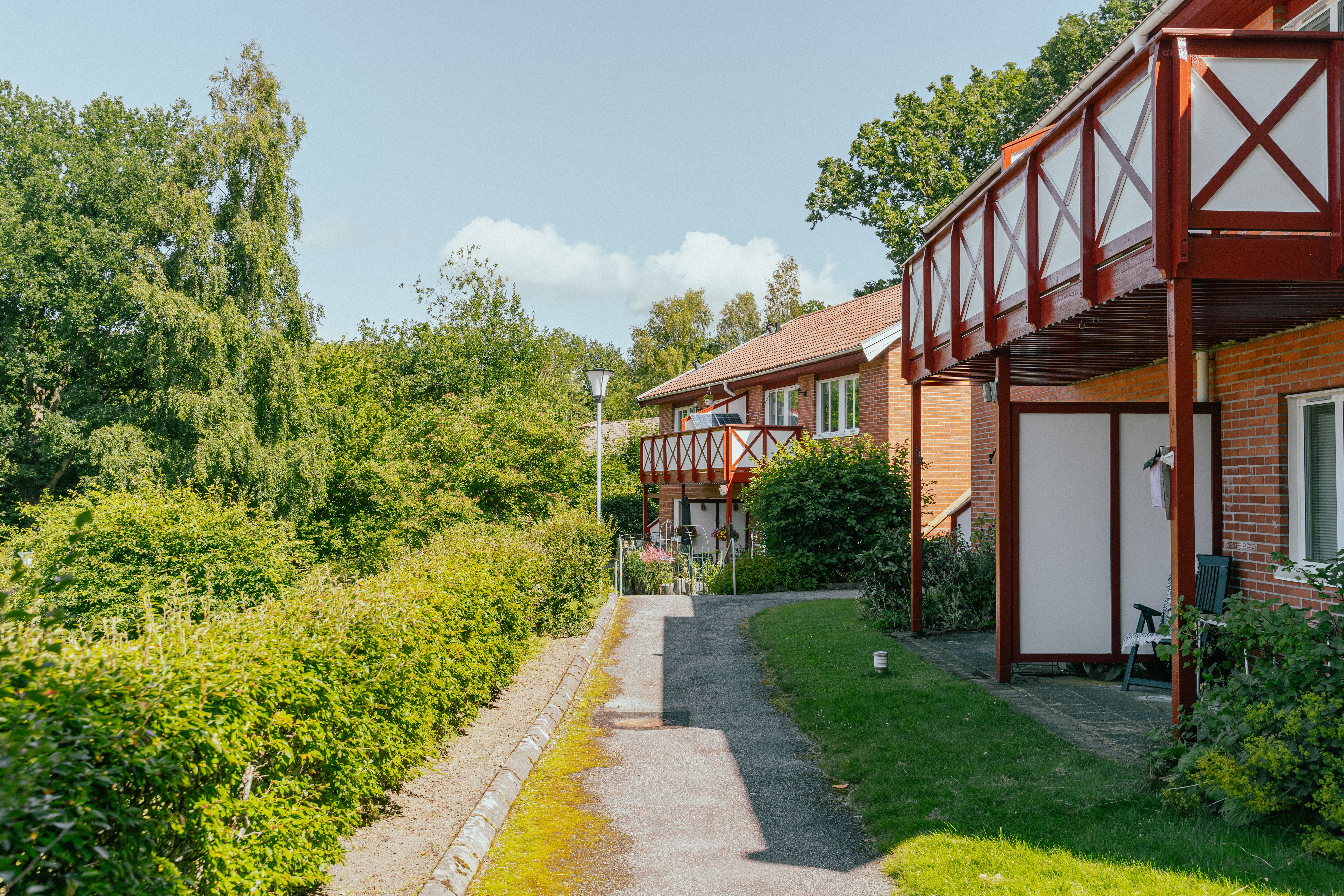 Tvåvåningshus med balkonger och uteplatser samt buskage på andra sidan