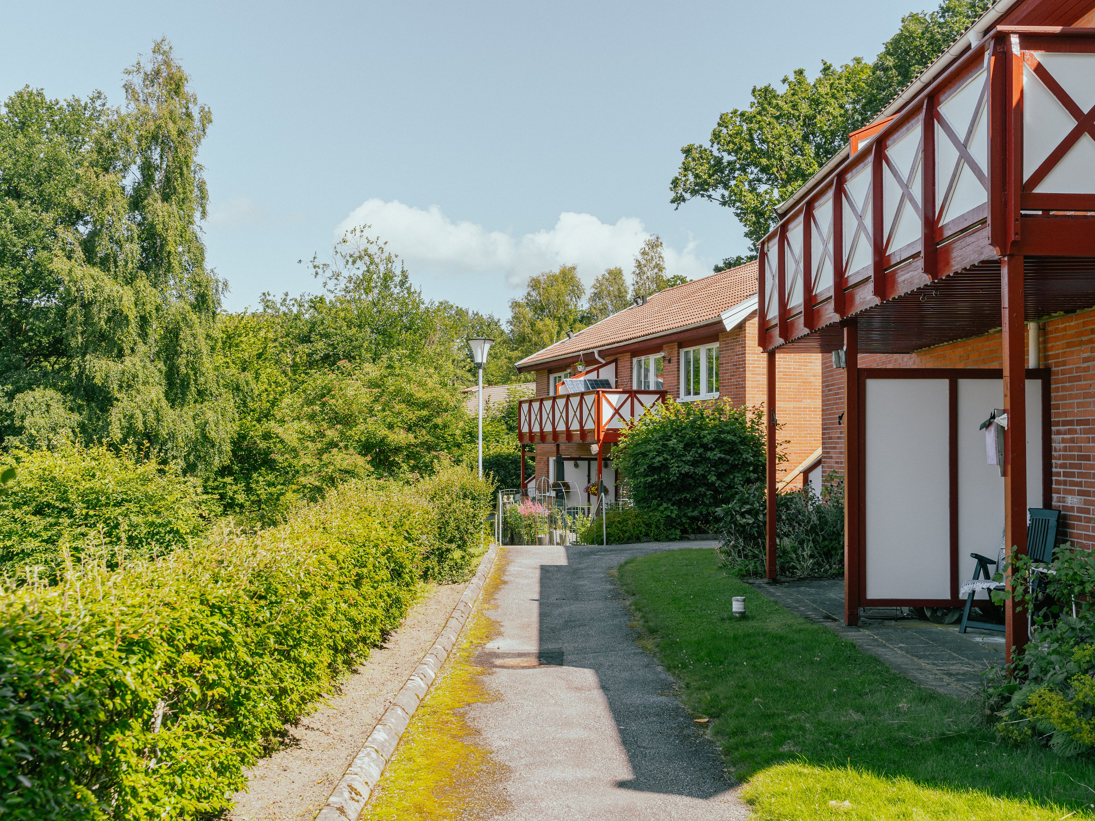 Tvåvåningshus med balkonger och uteplatser samt buskage på andra sidan
