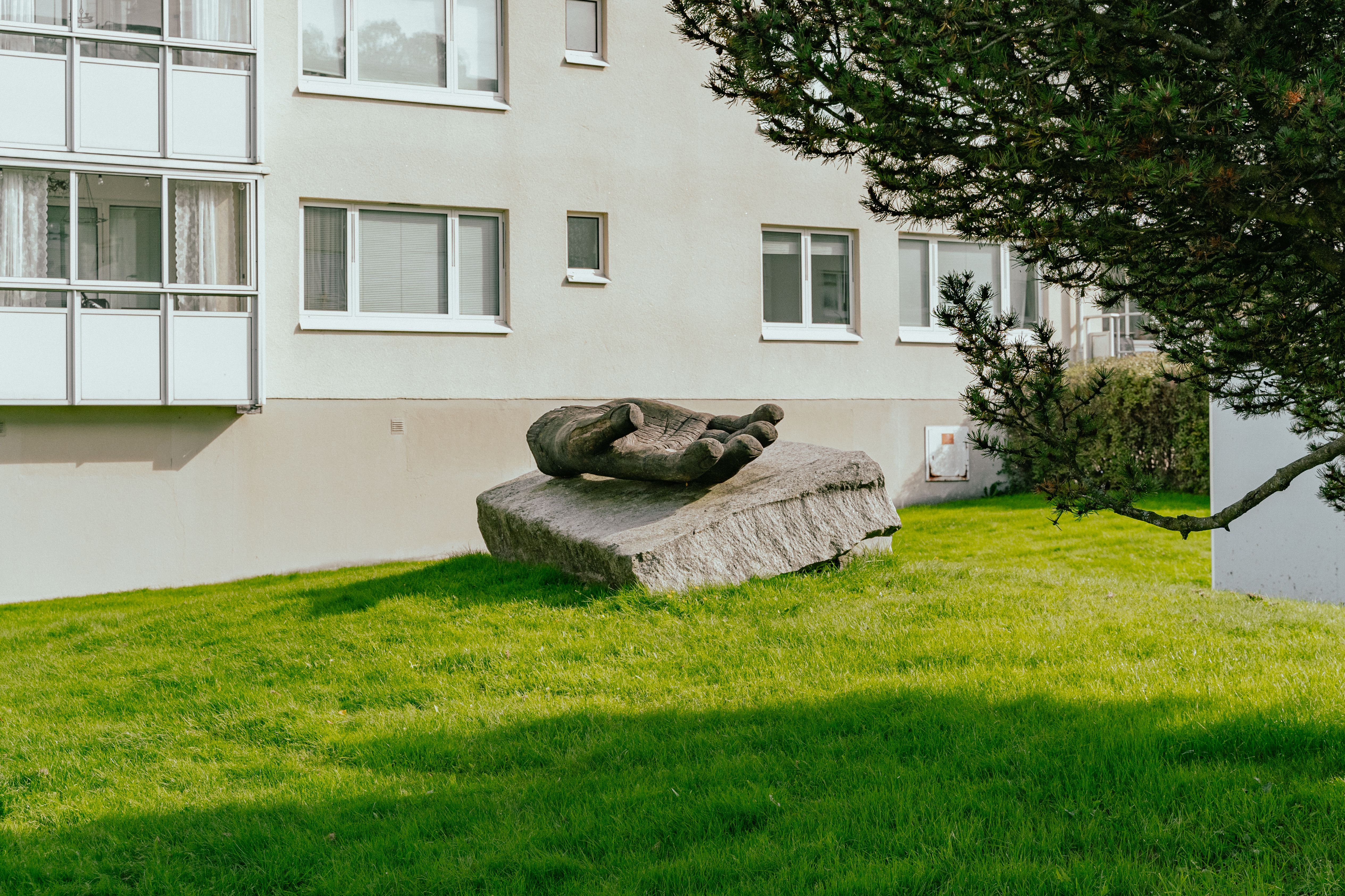 En stor hand uthuggen i trä placerad på ett stort stenblock, på en gräsmatta bredvid en fasad
