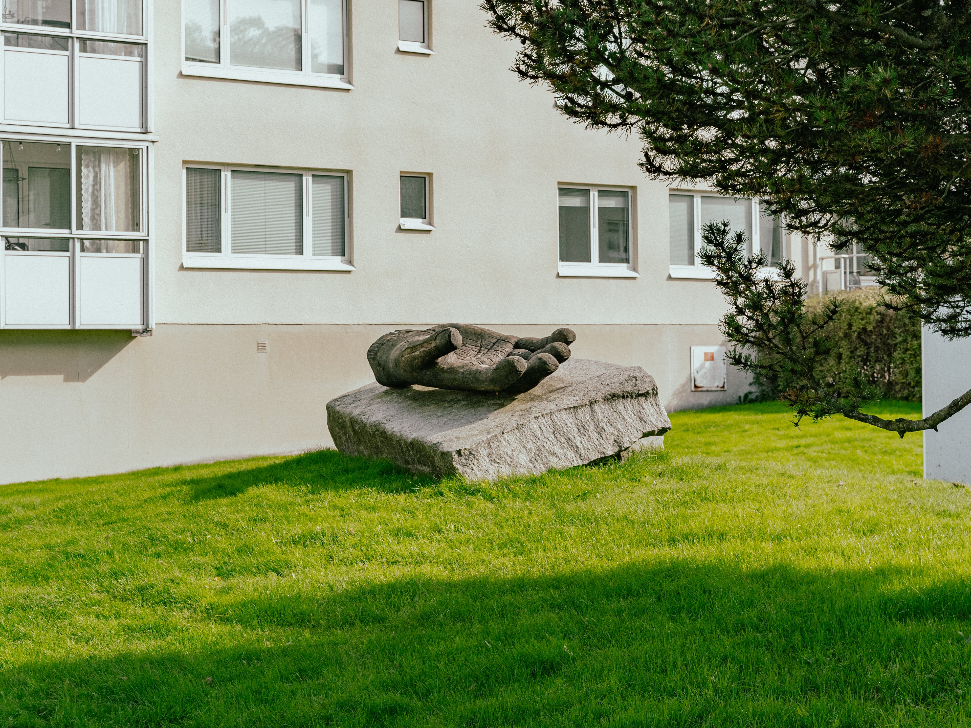 En stor hand uthuggen i trä placerad på ett stort stenblock, på en gräsmatta bredvid en fasad