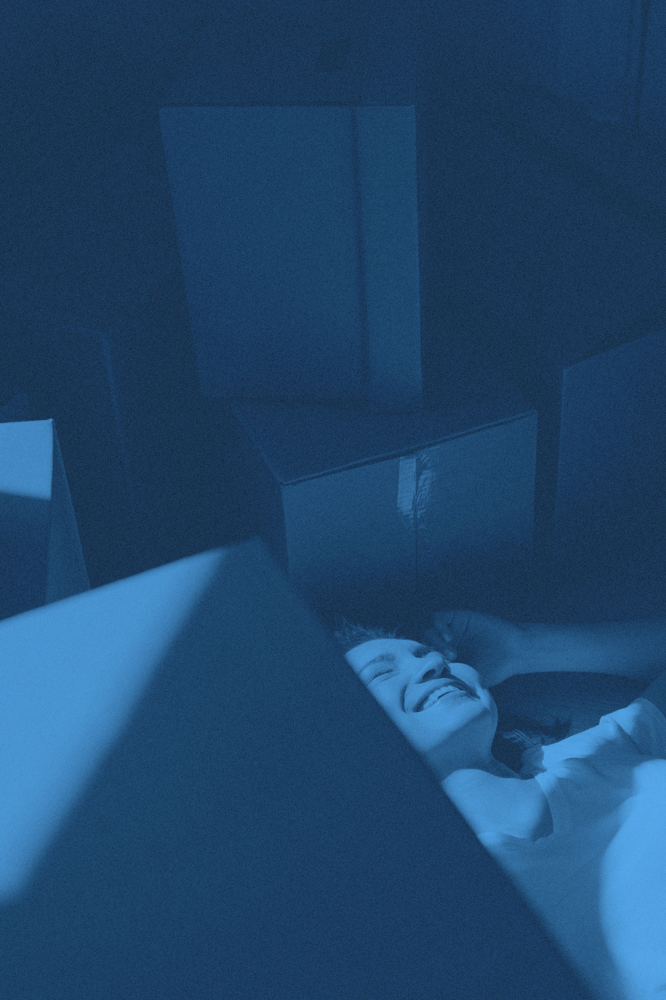 En person ligger på golvet omgiven av flyttkartonger