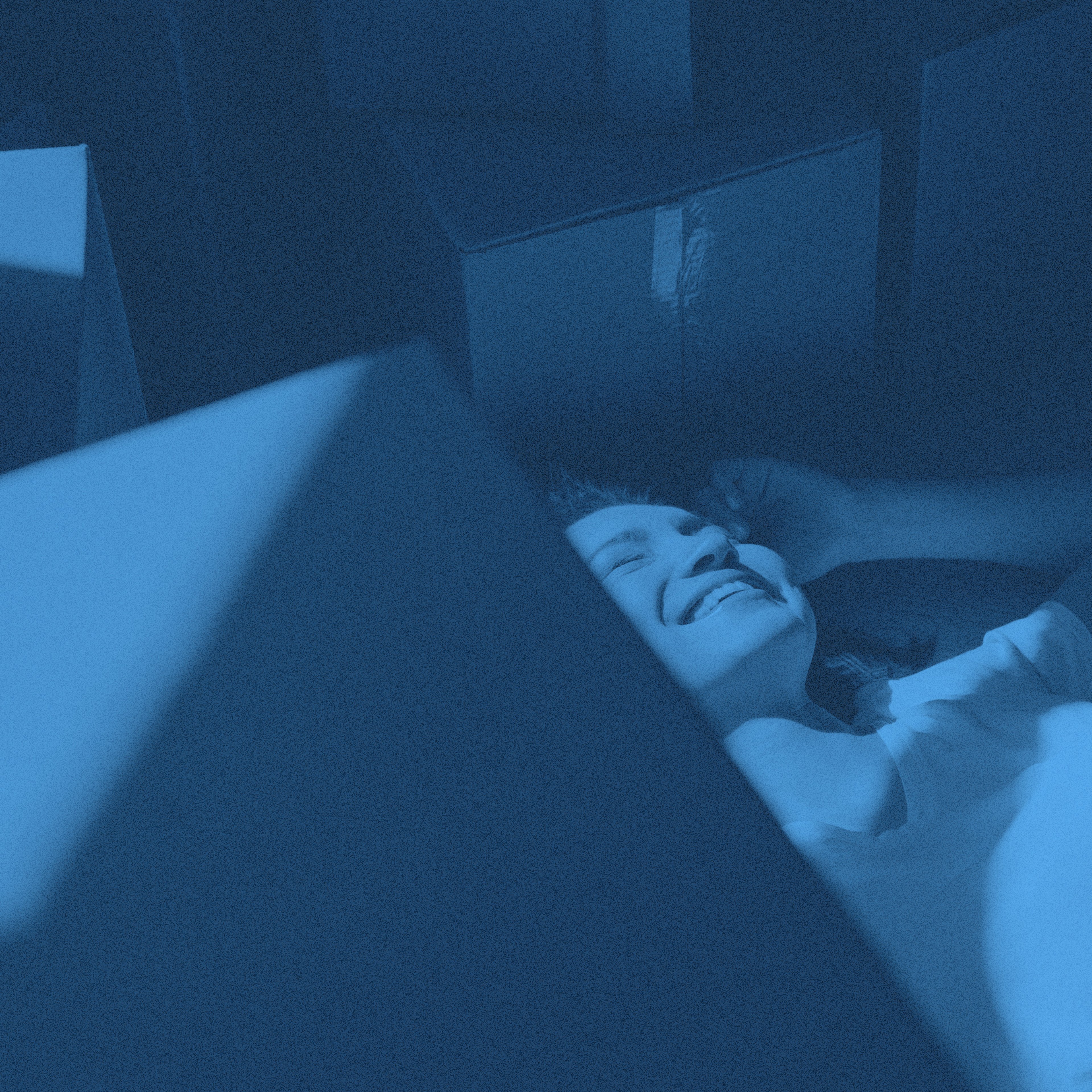 En person ligger på golvet omgiven av flyttkartonger