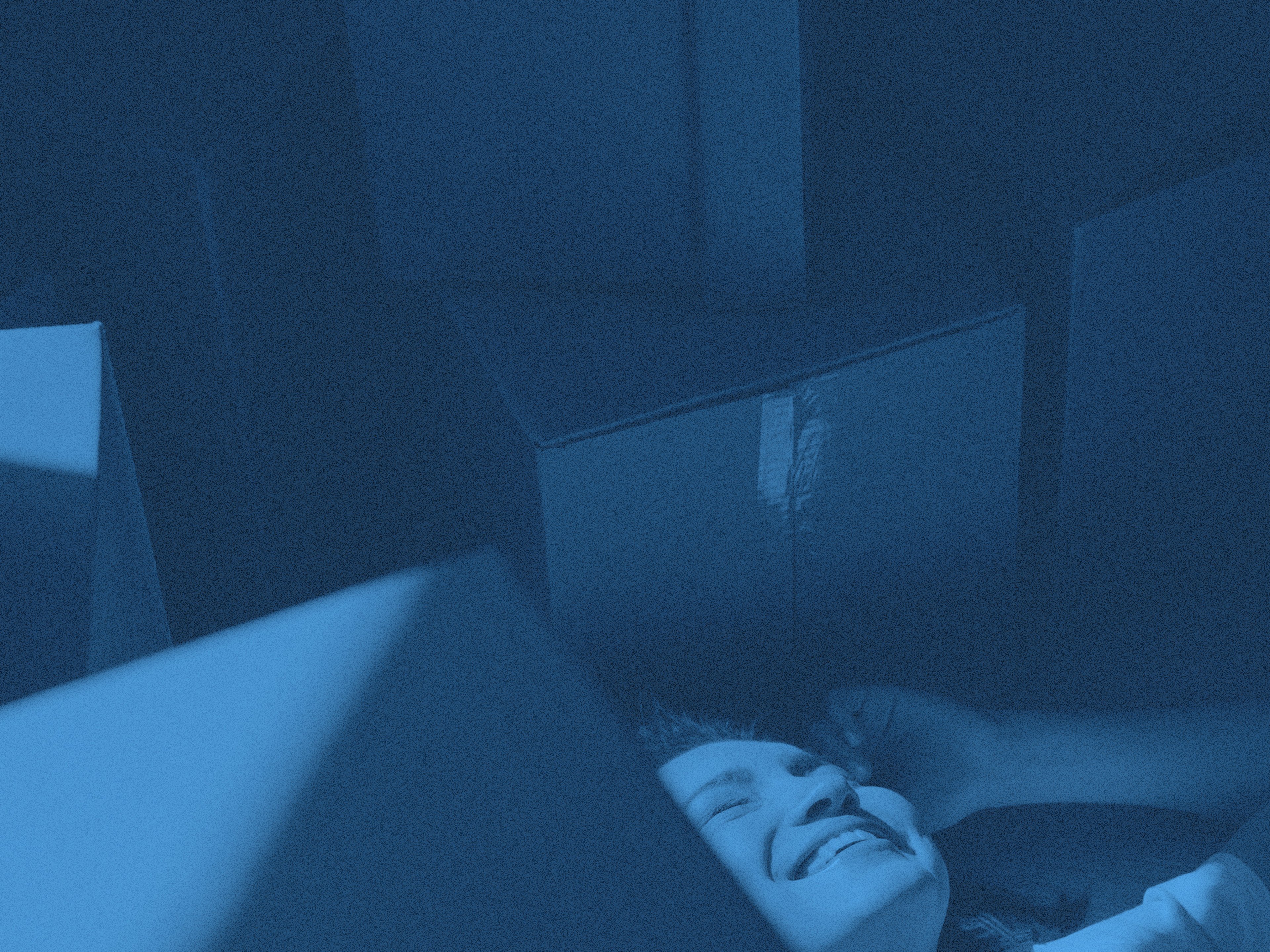 En person ligger på golvet omgiven av flyttkartonger