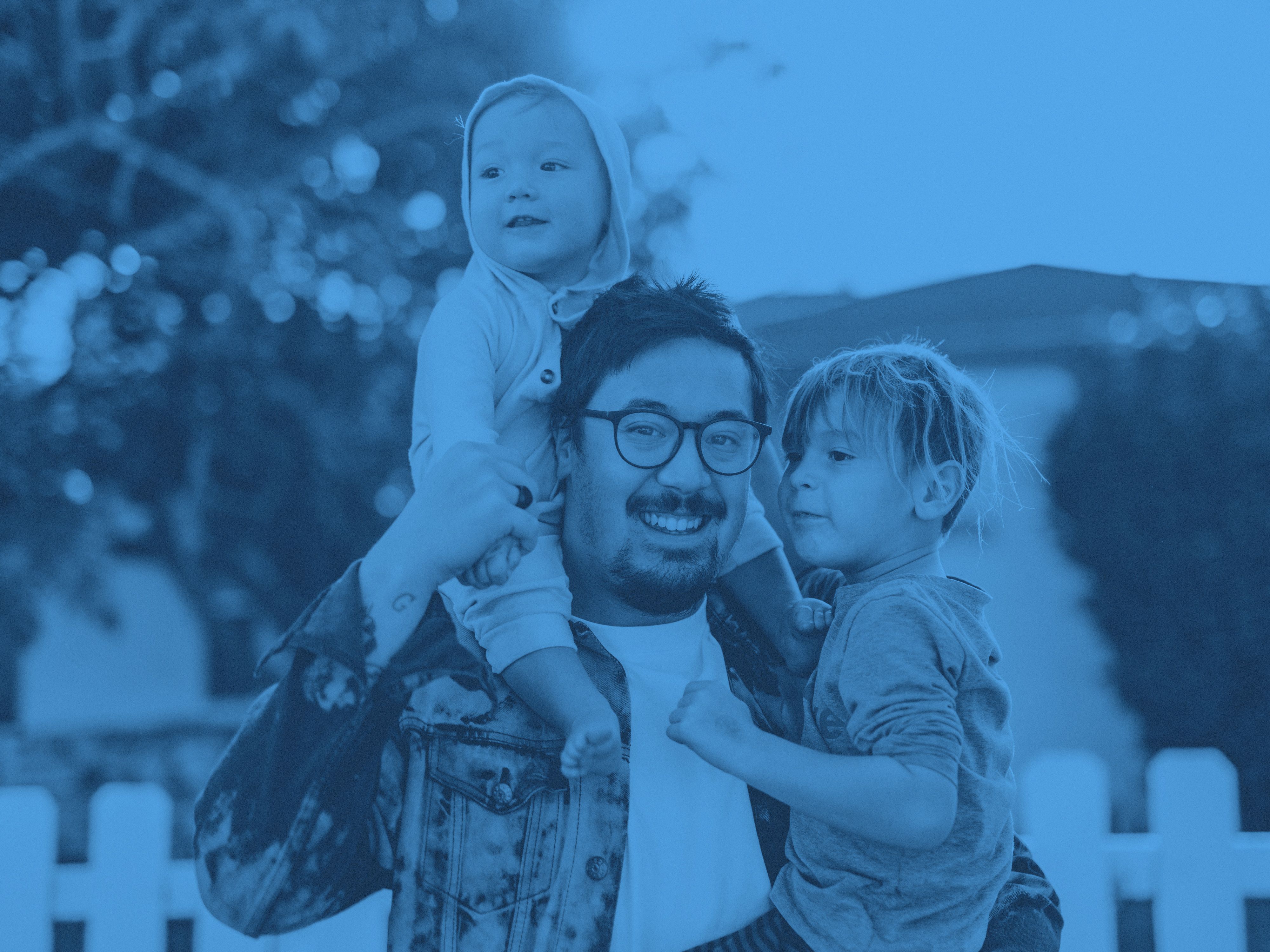 En pappa med ett bar i famnen och ett på axlarna