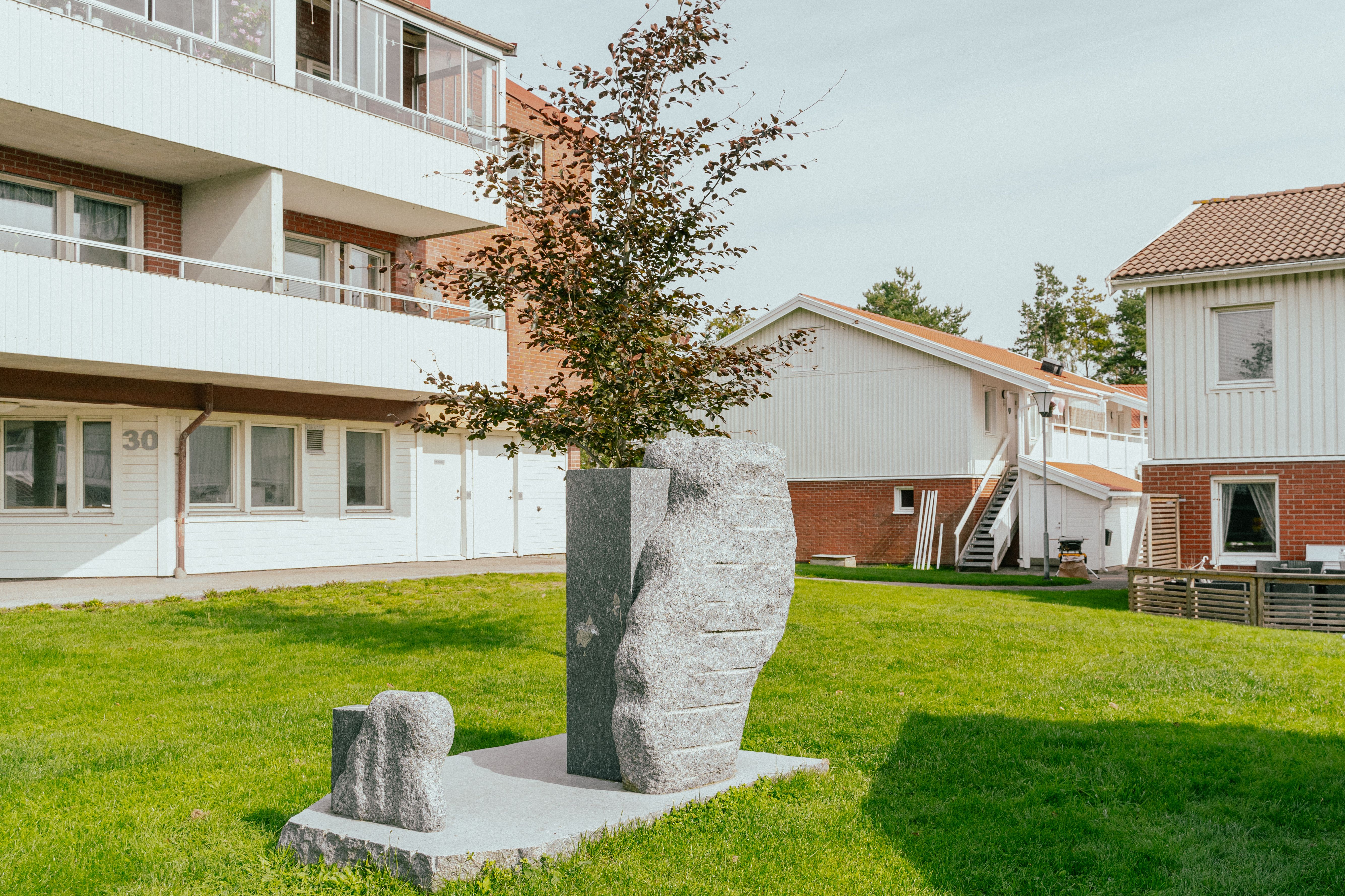 Ett konstverk i granit placerad på en gräsmatta mellan hus