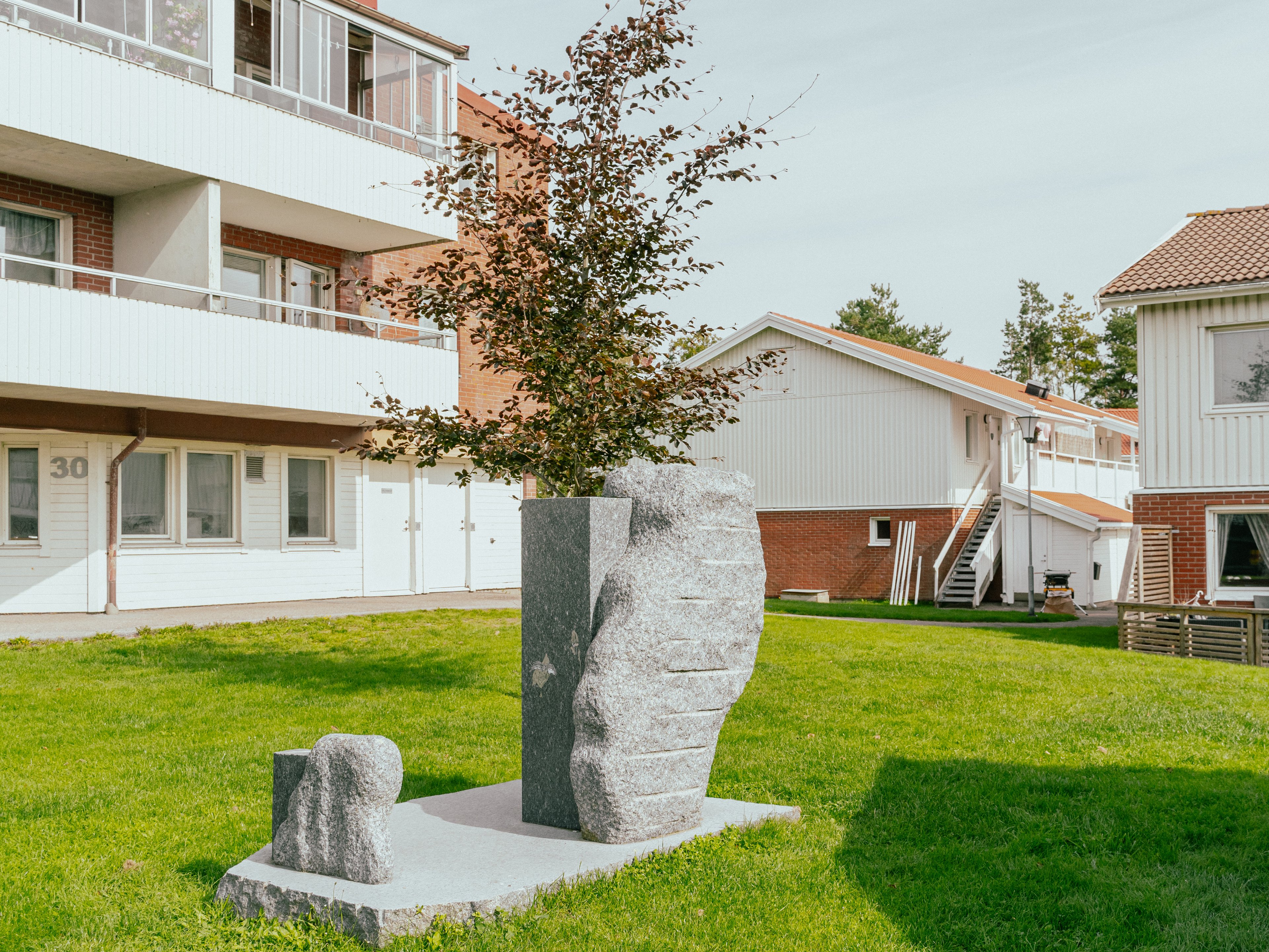 Ett konstverk i granit placerad på en gräsmatta mellan hus