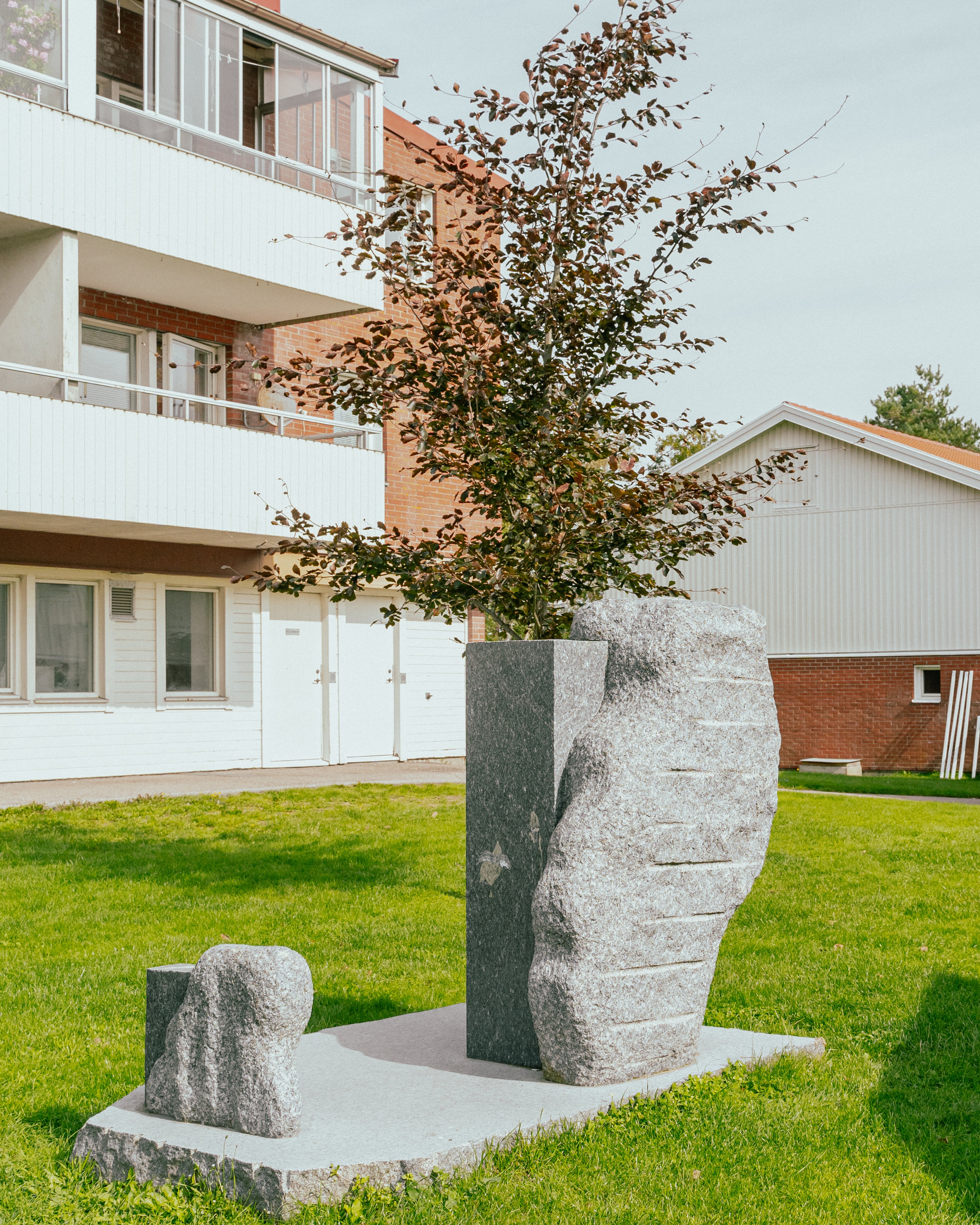 Ett konstverk i granit placerad på en gräsmatta mellan hus