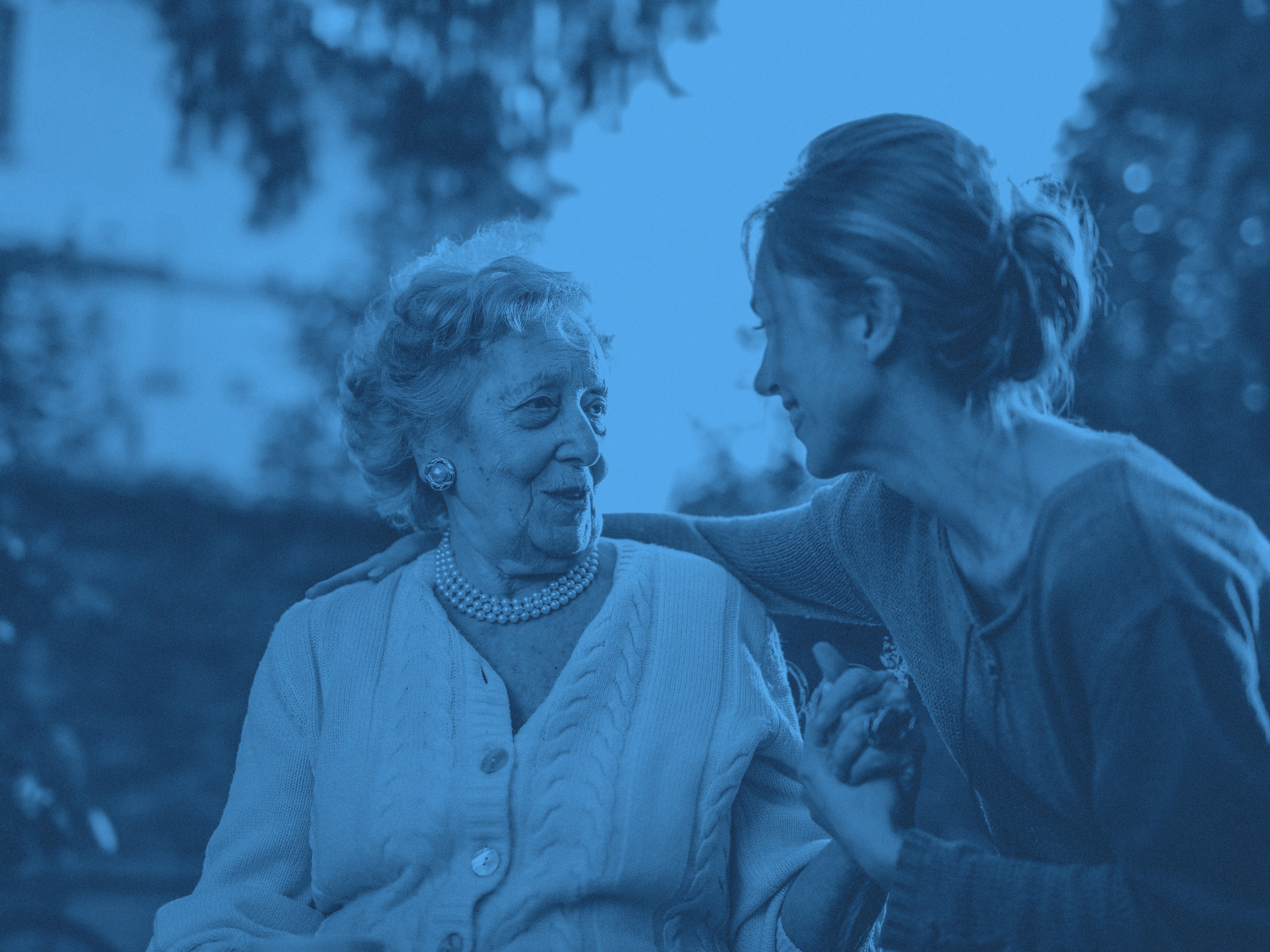 En äldre kvinna sitter på en bänk och samtalar med en yngre kvinna