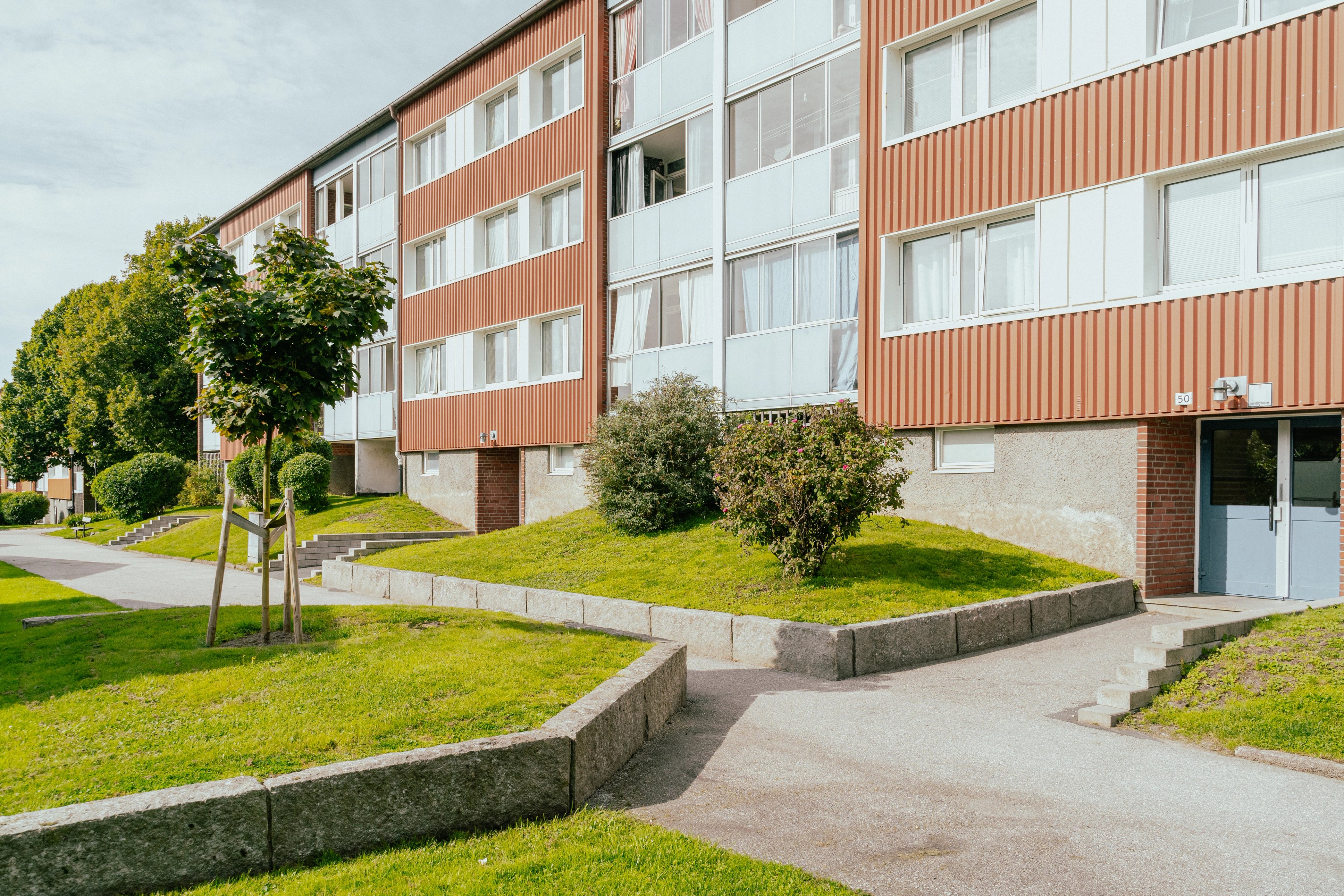 Husfasad med gräsmattor, träd och buskar framför