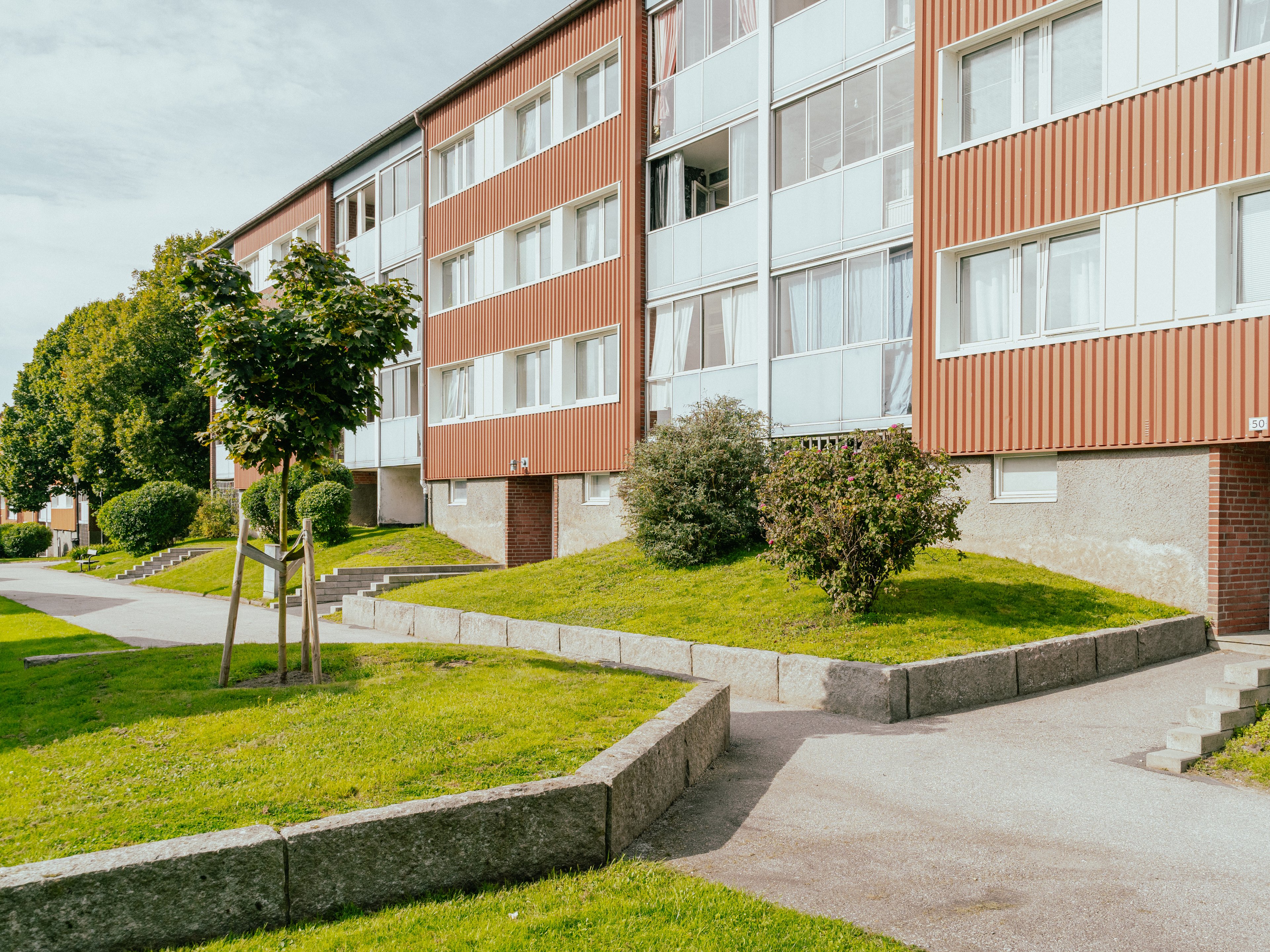 Husfasad med gräsmattor, träd och buskar framför