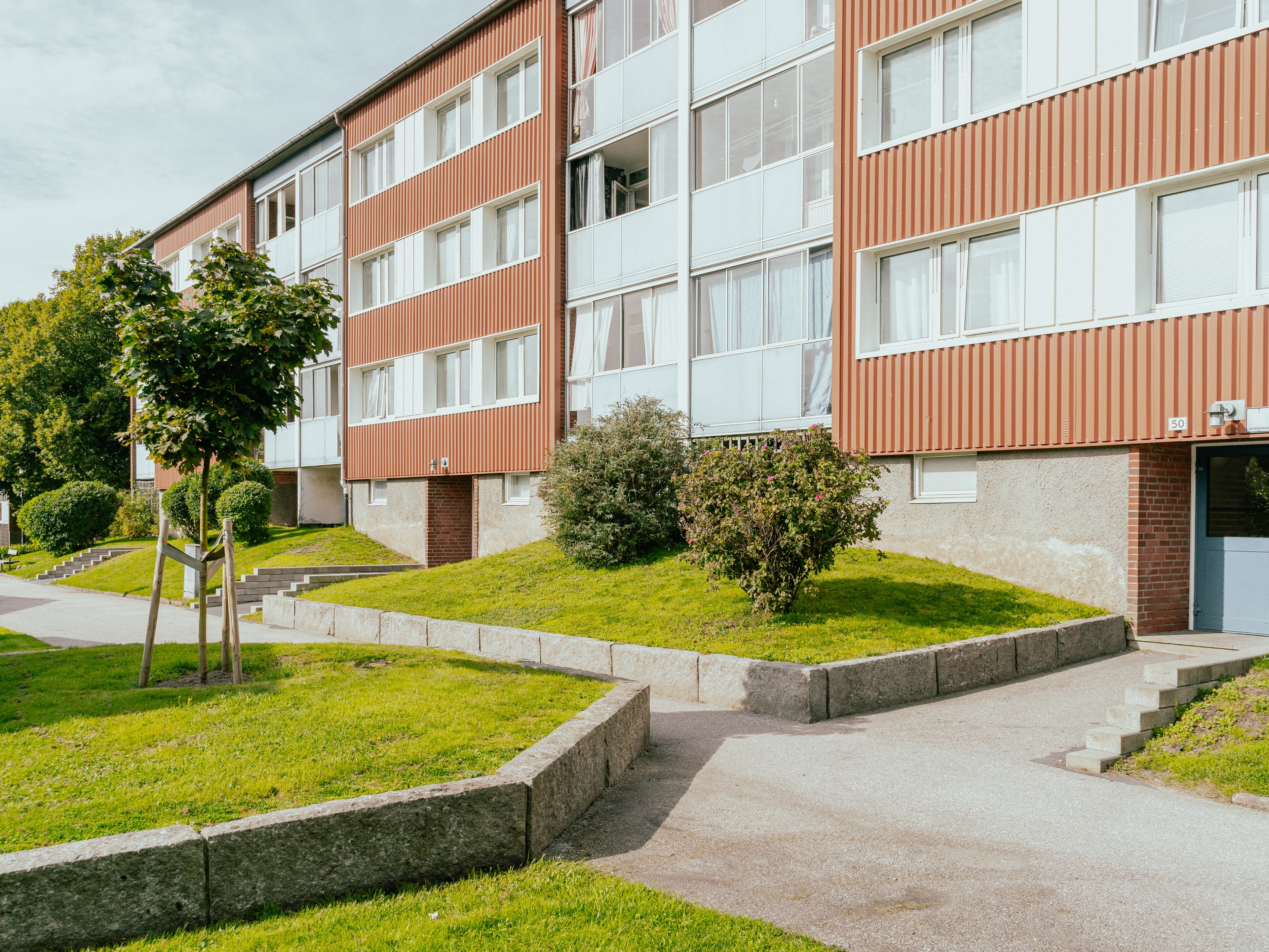 Husfasad med gräsmattor, träd och buskar framför