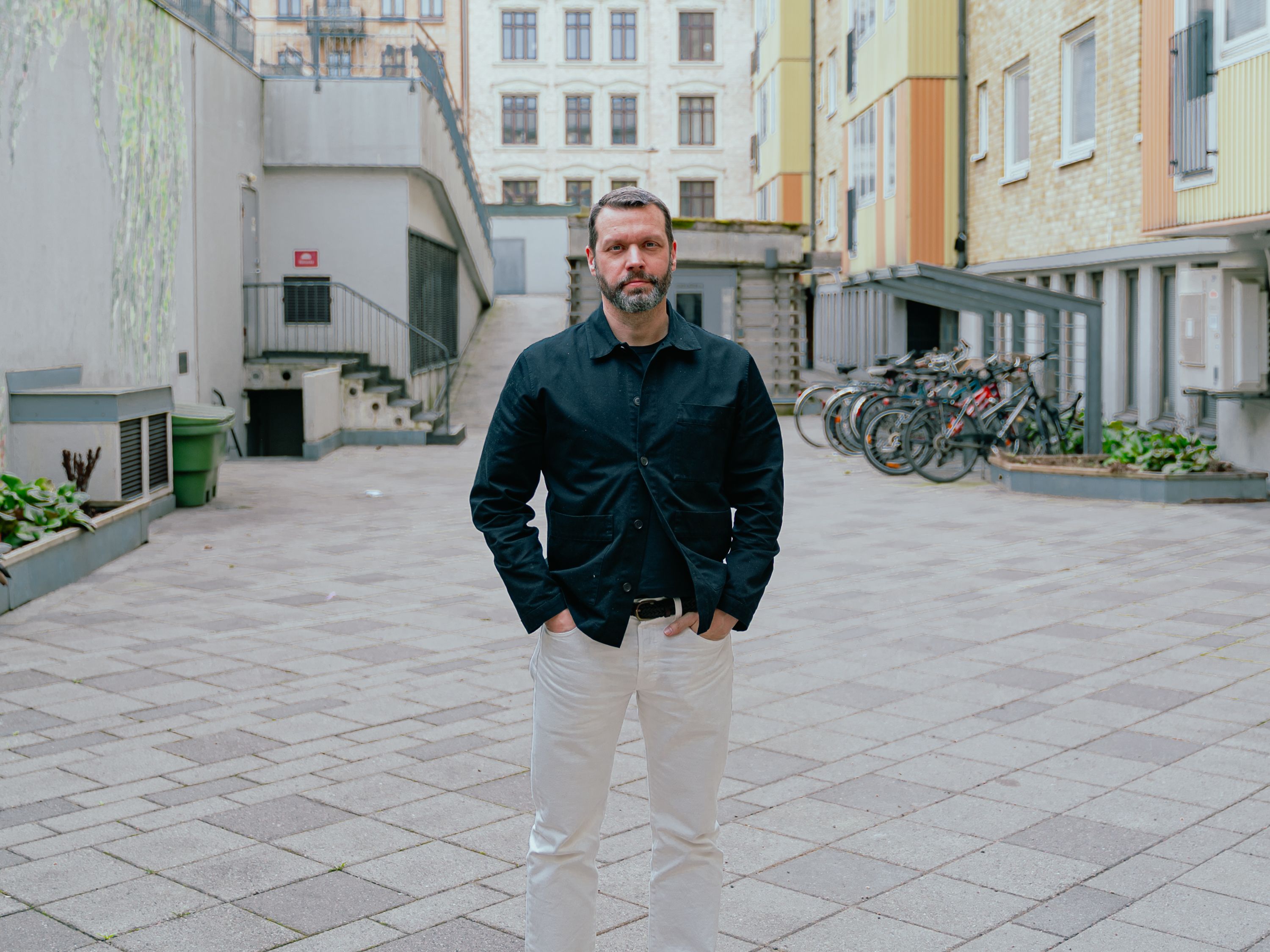 En  man tittar in i kameran med en innegård i bakgrunden