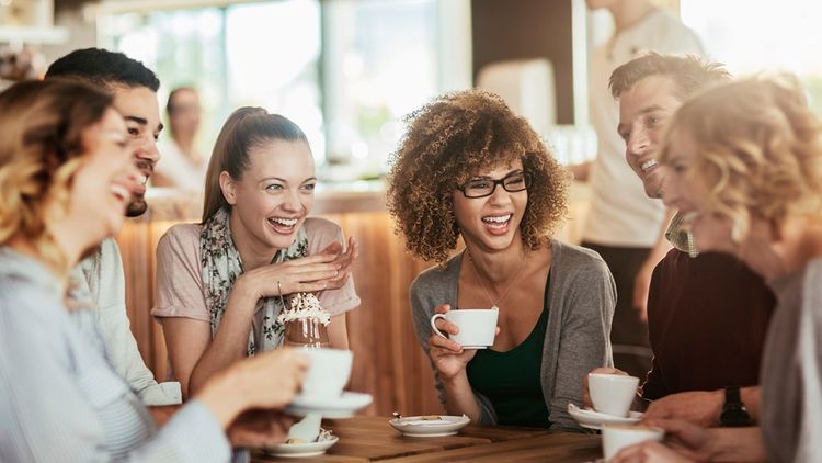 Group of smiling women and men friends cheerfully enjoying coffees at a café